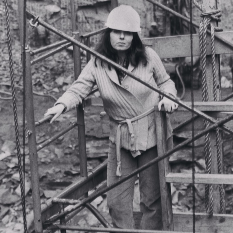 A black-and-white photograph of Barbara Res, the first woman to lead a skyscraper construction project. As the head of the Trump Tower project in the 1980s, steel beams in front of her. Women in Hard hat, PPE for construction safety.